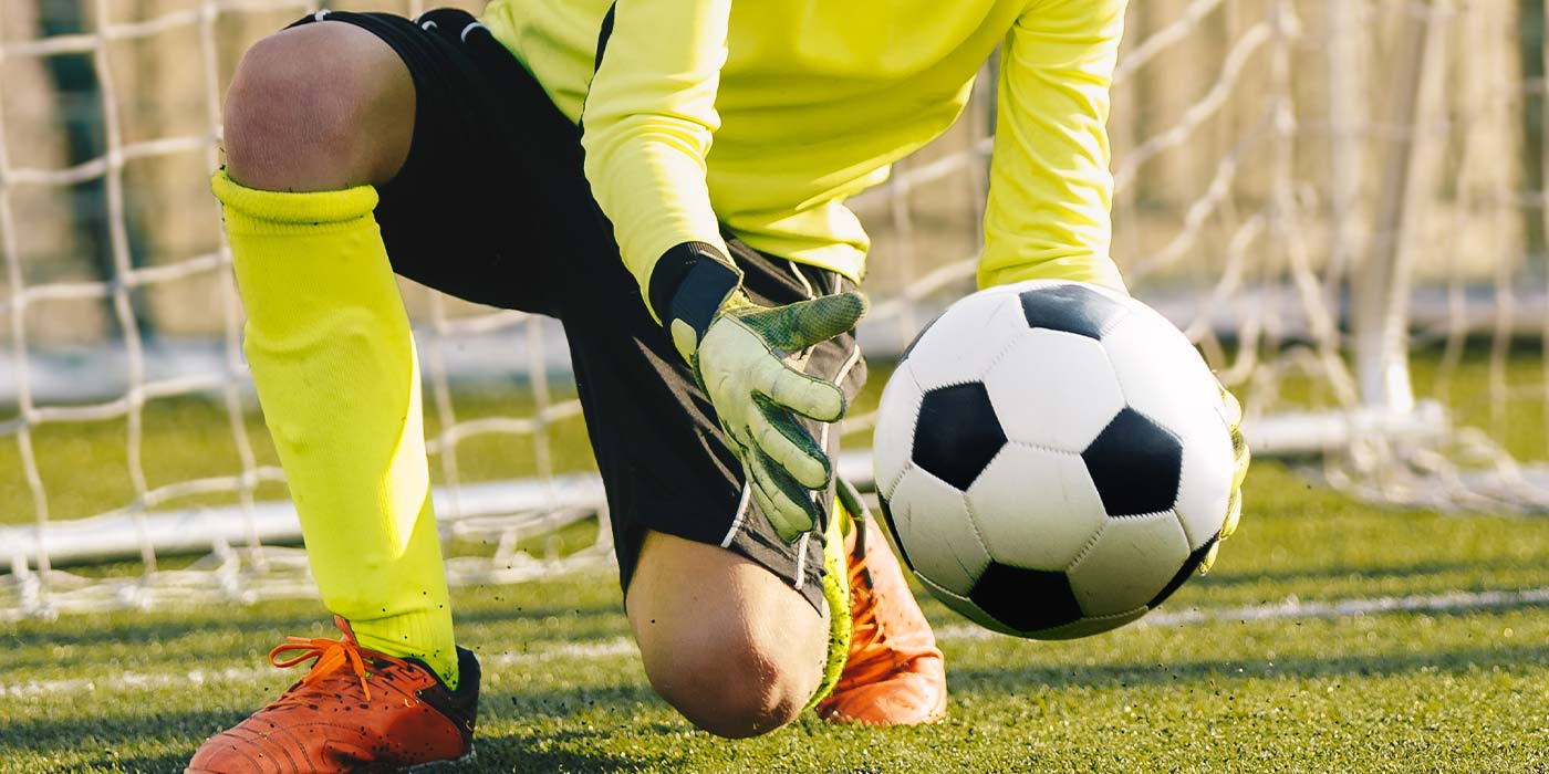 Kinder spielen Fußball, Jugendmannschaft, TorwartIn fängt den Ball kniend auf