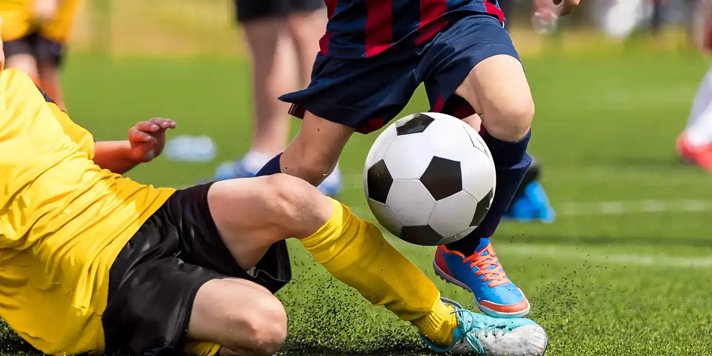Kinder spielen Fußball, Jugendmannschaft, SpielerIn versucht den Ball wegzuschießen