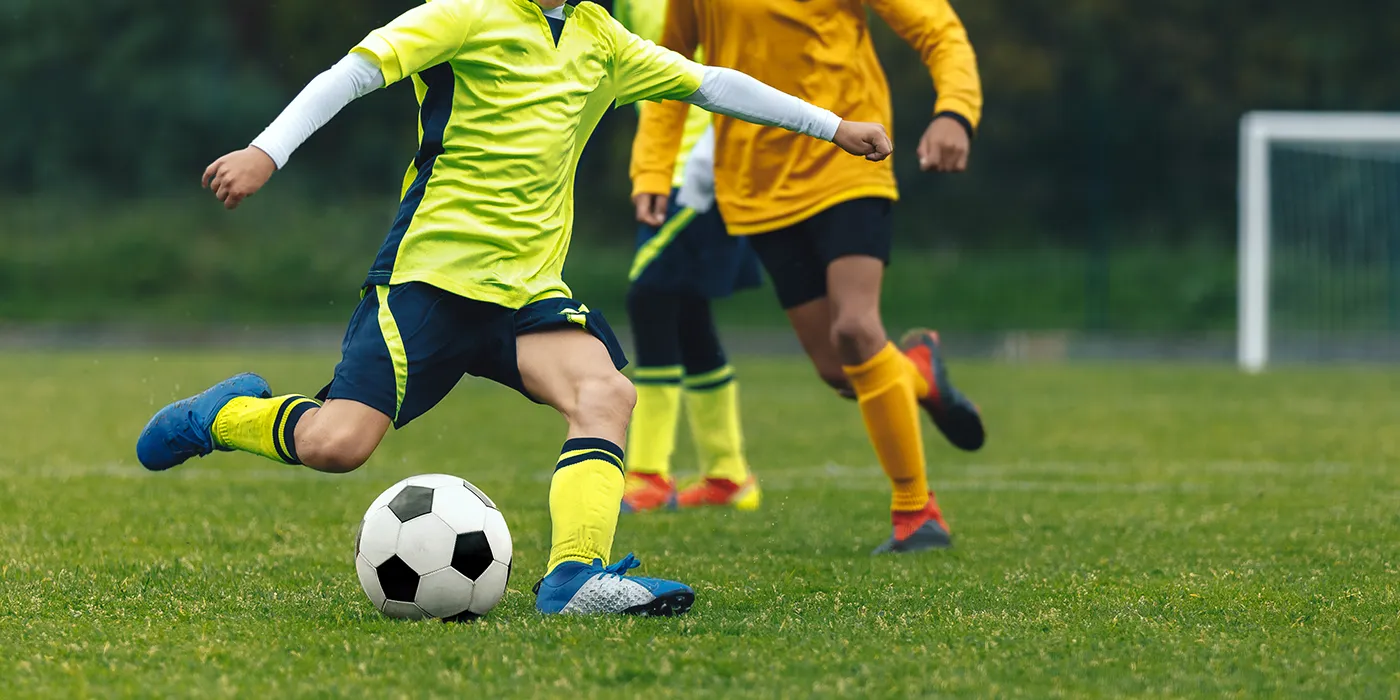 Kinder spielen Fußball, Jugendmannschaft, ein Kind in gelbem Trikot schießt den Ball